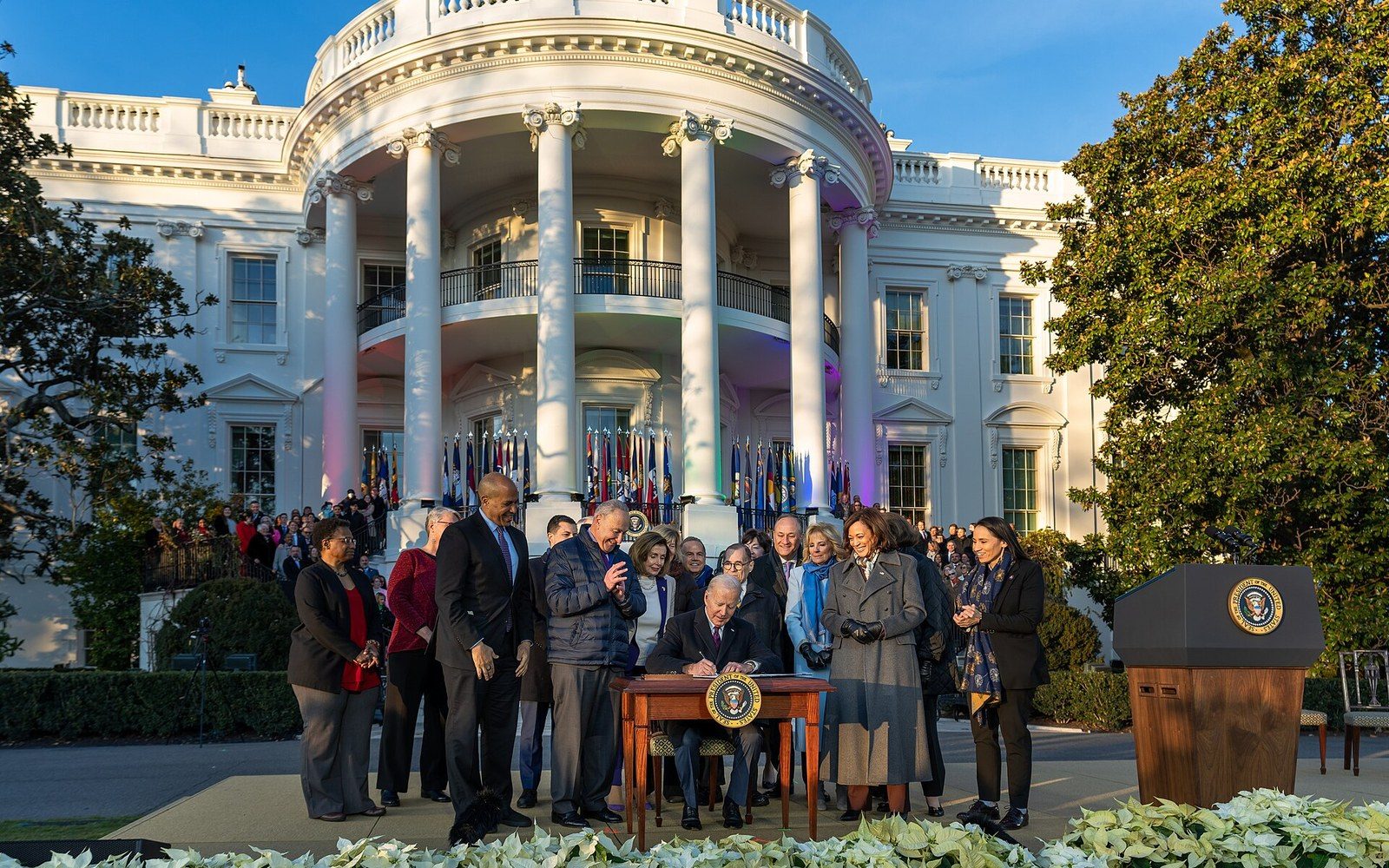 President signing legislation at an outdoor desk on the White House South Lawn as officials look on